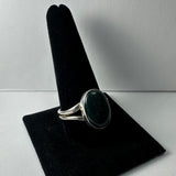 Silver ring with a smooth, oval green serpentine stone set on a split band, displayed on a black velvet ring holder against a neutral background.