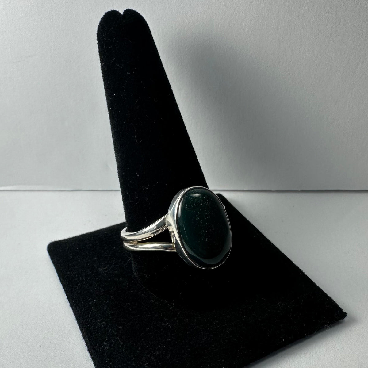 Silver ring with a smooth, oval green serpentine stone set on a split band, displayed on a black velvet ring holder against a neutral background.