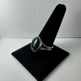 Silver ring with a polished deep green serpentine stone, displayed vertically on a black velvet ring holder against a plain white background.
