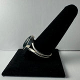 Silver ring with a polished green serpentine cabochon set in a smooth bezel, displayed on a black velvet finger stand against a plain background.