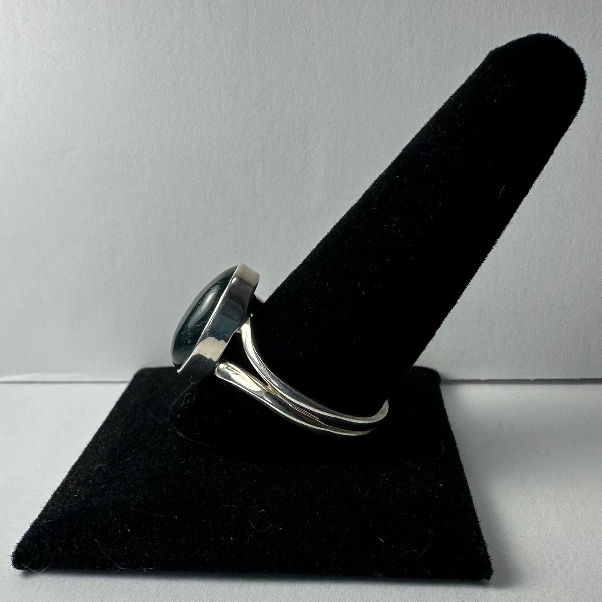 Silver ring with a polished green serpentine cabochon set in a smooth bezel, displayed on a black velvet finger stand against a plain background.