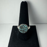 Round Tibetan turquoise ring with a silver band and a mottled blue and black stone set in a circular bezel, displayed on a black velvet holder.
