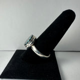 Silver ring with a large oval Tibetan turquoise stone set in a hammered bezel, displayed on a black velvet ring holder against a plain white background.