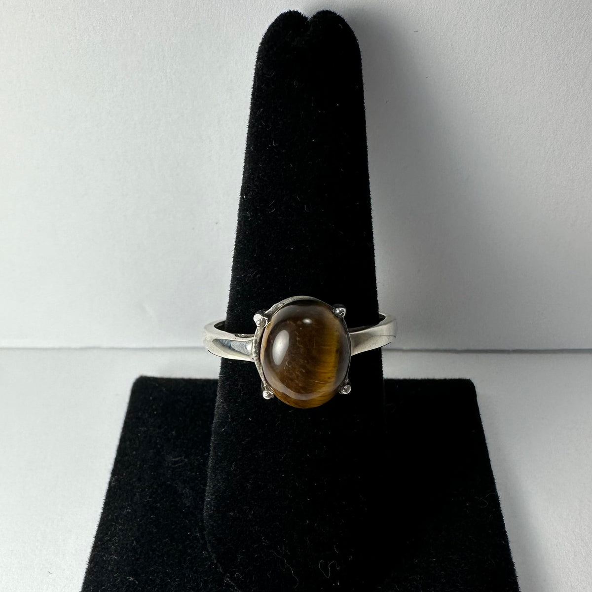 Silver ring with oval polished tiger eye gemstone set on a black velvet ring display stand, photographed against a light gray background.
