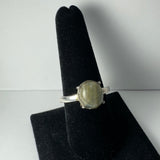 Silver ring with a round, translucent labradorite stone set in four prongs, displayed upright on a black velvet finger-shaped stand against a white background.
