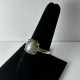 Silver ring with a round labradorite stone showing blue and green iridescence, displayed on a black velvet finger stand against a white background.