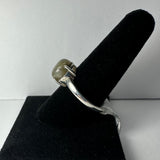 Silver ring featuring a polished labradorite cabochon with subtle gray and green hues, displayed on a black velvet ring holder against a plain white background.