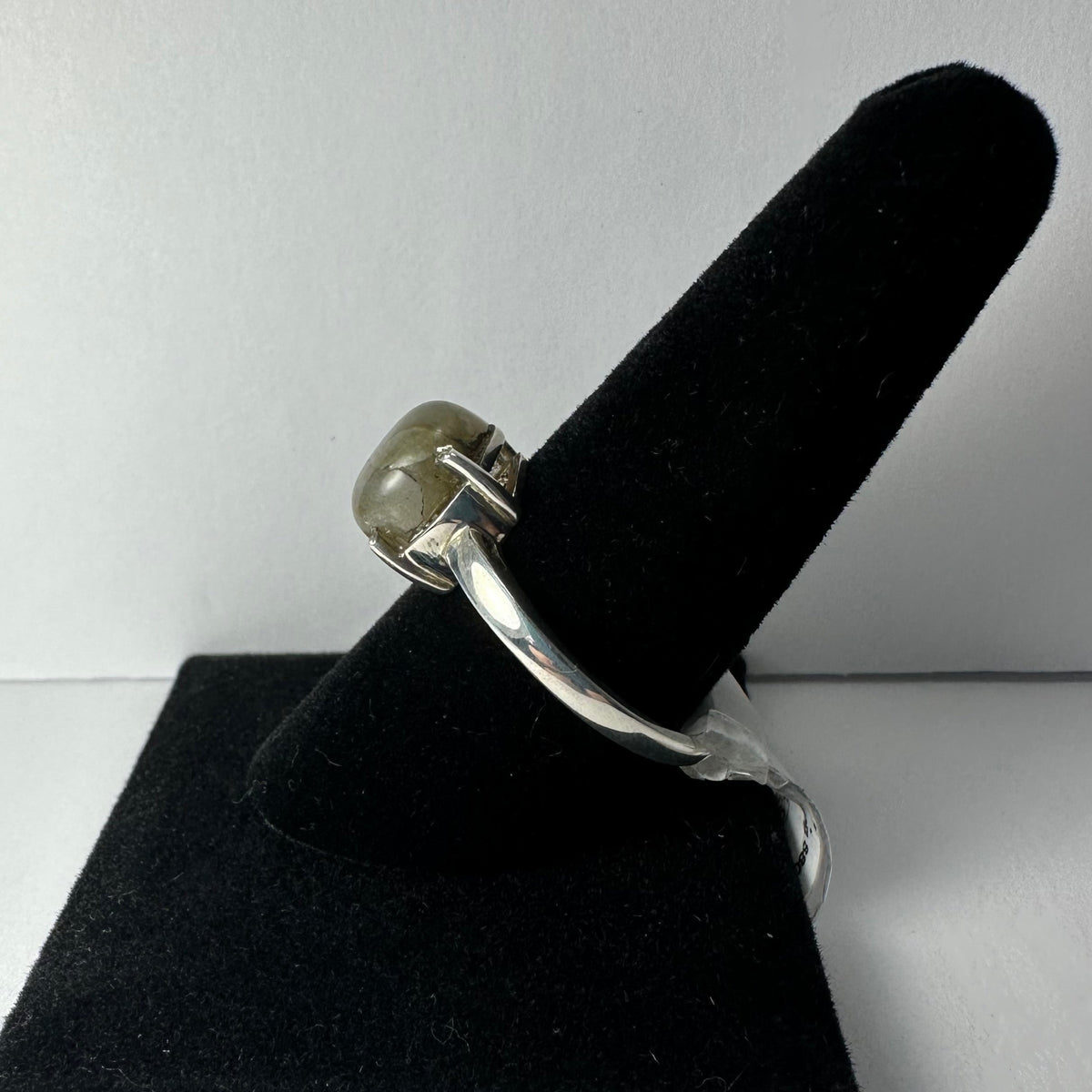 Silver ring featuring a polished labradorite cabochon with subtle gray and green hues, displayed on a black velvet ring holder against a plain white background.