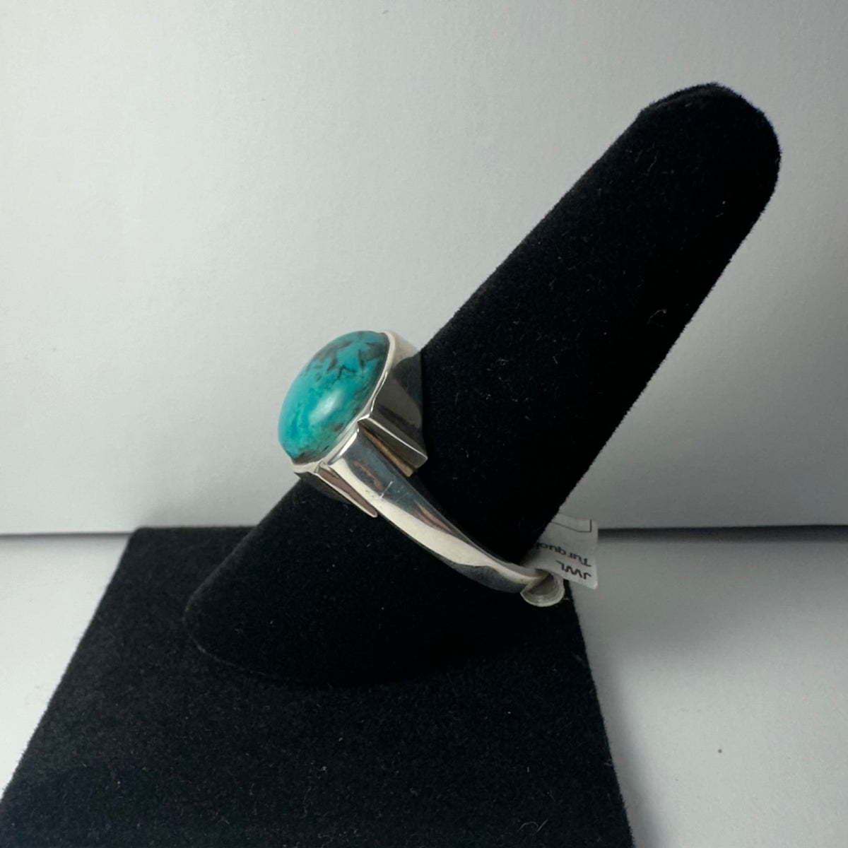 Silver ring with a round turquoise stone set in a bezel, displayed on a black ring stand against a plain white background.