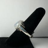 Silver ring featuring a round, polished moonstone cabochon set in a thick bezel, displayed on a black velvet ring holder against a plain white background.