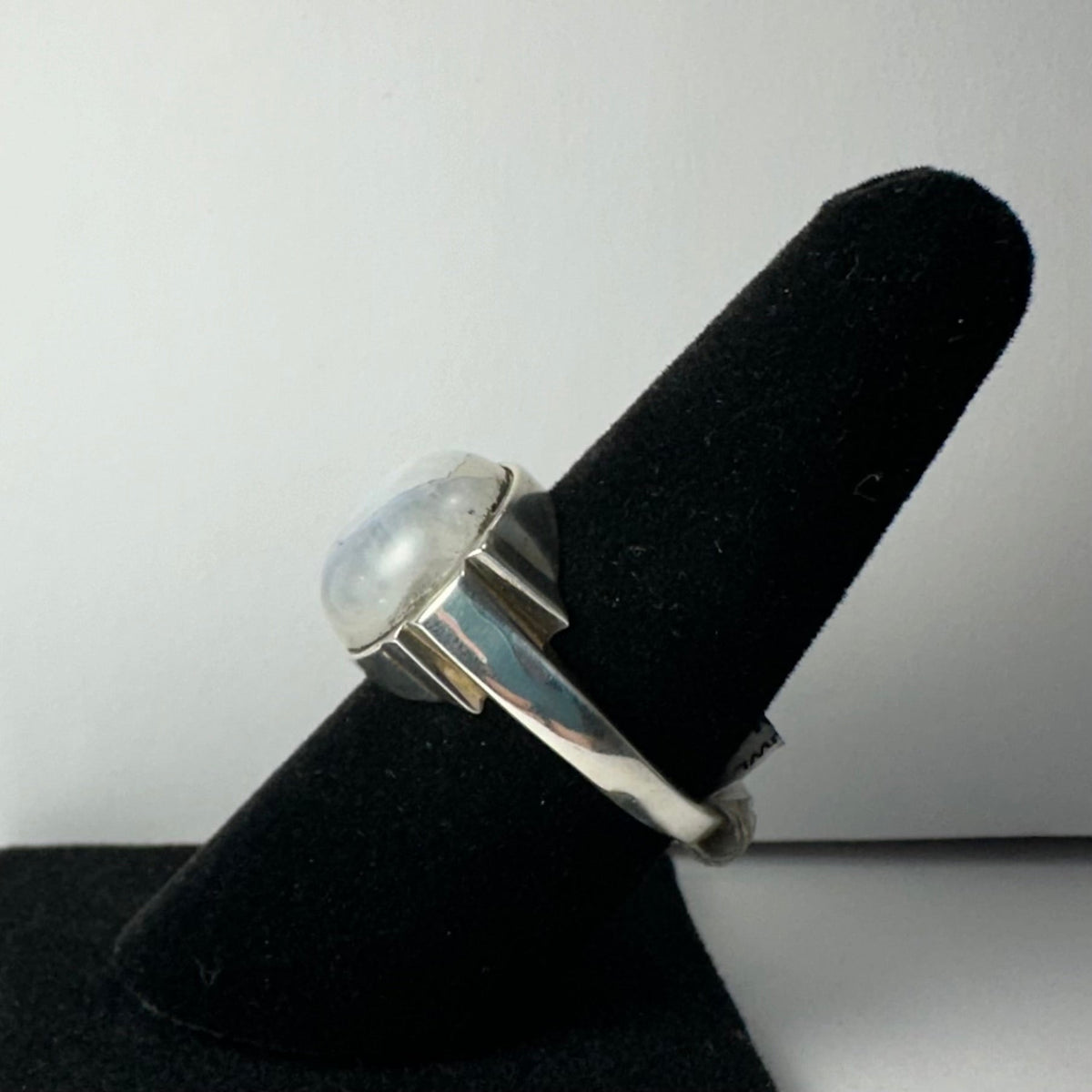 Silver ring featuring a round, polished moonstone cabochon set in a thick bezel, displayed on a black velvet ring holder against a plain white background.