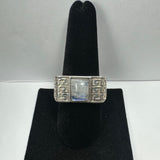 Silver ring with a rectangular moonstone center and intricate geometric patterns on the band, displayed on a black velvet ring stand.