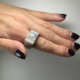 Hand with dark purple glossy nail polish wearing a silver ring featuring a rectangular moonstone and Greek key pattern on the band.