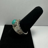 Silver ring with ornate detailed band featuring small raised dots and a smooth turquoise oval stone on top, displayed on a black velvet cone stand.