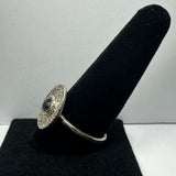 Silver ring with a textured, circular face and a central dark blue iolite gemstone displayed on a black velvet ring holder against a plain background.