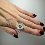 Silver ring with a hammered circular face featuring a central round dark blue iolite stone, worn on a finger with black-to-clear ombré polished nails.
