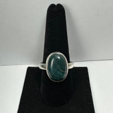 Silver ring with an oval deep green serpentine stone set in a simple bezel, displayed on a black velvet ring holder.
