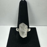 Silver ring with a large, irregular-shaped rough quartz stone mounted on a black velvet ring display stand against a white background.