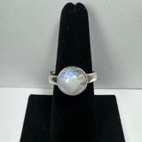Silver ring with a round polished moonstone cabochon showing blue and white iridescence, displayed vertically on a black velvet stand against a gray background.