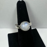 Silver ring with a round, translucent moonstone exhibiting a subtle blue sheen, displayed on a black velvet finger stand against a plain background.