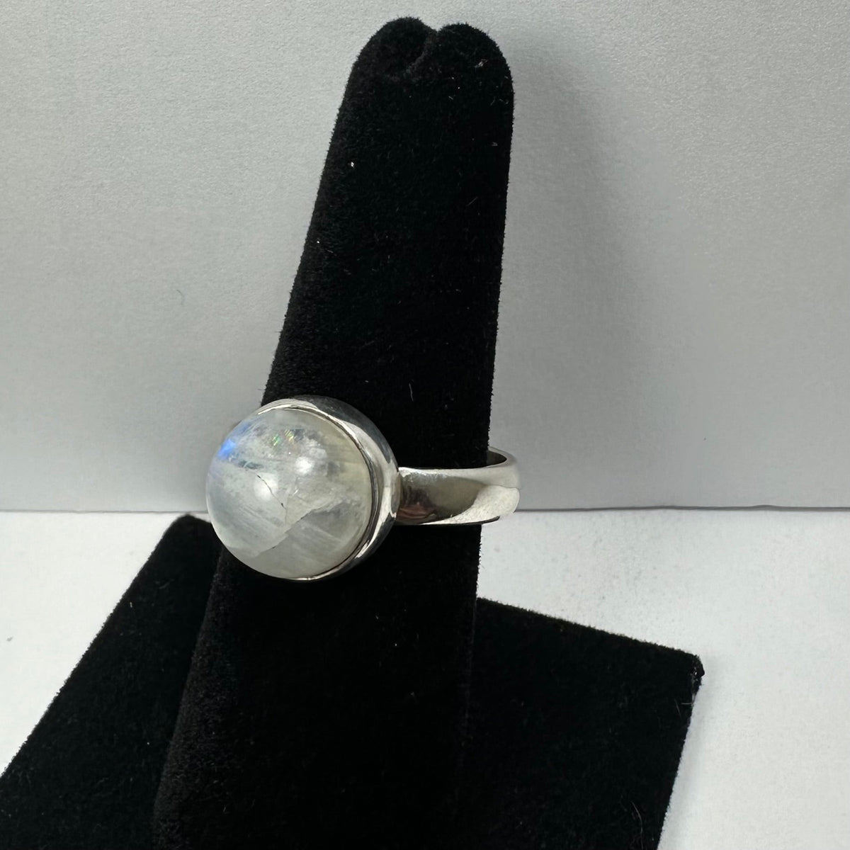 Moonstone ring with a rounded translucent white-blue stone set in a simple polished silver band, displayed on a black velvet ring holder.
