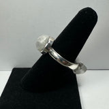 Silver ring with a round translucent moonstone set in a bezel, displayed on a black ring holder against a light gray background.