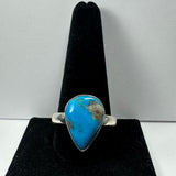 Silver ring with a teardrop-shaped vivid turquoise stone featuring natural brown matrix, displayed upright on a black velvet ring holder.
