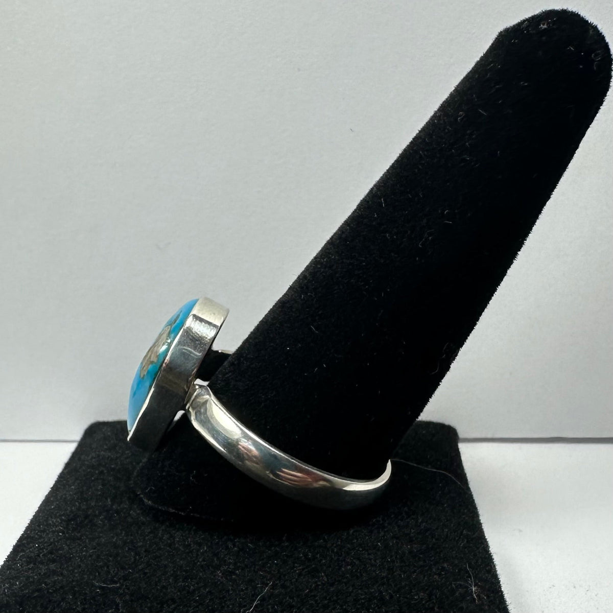 Silver ring with a large oval turquoise stone set in a smooth bezel, displayed on a black velvet ring holder against a white background.