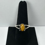 Silver ring with an oval polished tiger eye stone, displayed upright on a black velvet ring holder against a plain light background.