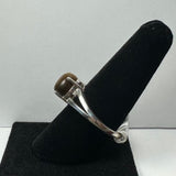 Silver ring with a polished brown tiger eye stone mounted on a black velvet cone display against a plain white background