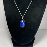 Oval lapis lazuli pendant with deep blue and gold flecks on a silver chain, displayed on black velvet jewelry bust.