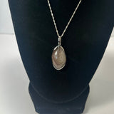 Teardrop-shaped silver pendant with fine rutile inclusions, hanging from a delicate twisted silver chain on a black display stand.