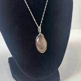 Teardrop-shaped silver pendant with rutile inclusions on a twisted silver chain, displayed against a black velvet bust.