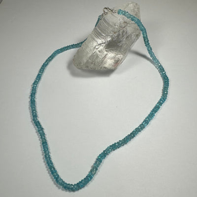Natural Blue Apatite Necklace displayed on a dark blue fabric background and worn close-up, highlighting the vivid blue stone and sterling silver clasp.