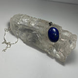 Oval lapis lazuli pendant with deep blue and gold flecks hanging on a delicate silver chain, displayed draped over a textured clear quartz crystal.