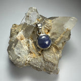 Round cut Tanzanite pendant with .925 Sterling Silver clasp displayed on a dark textured background
