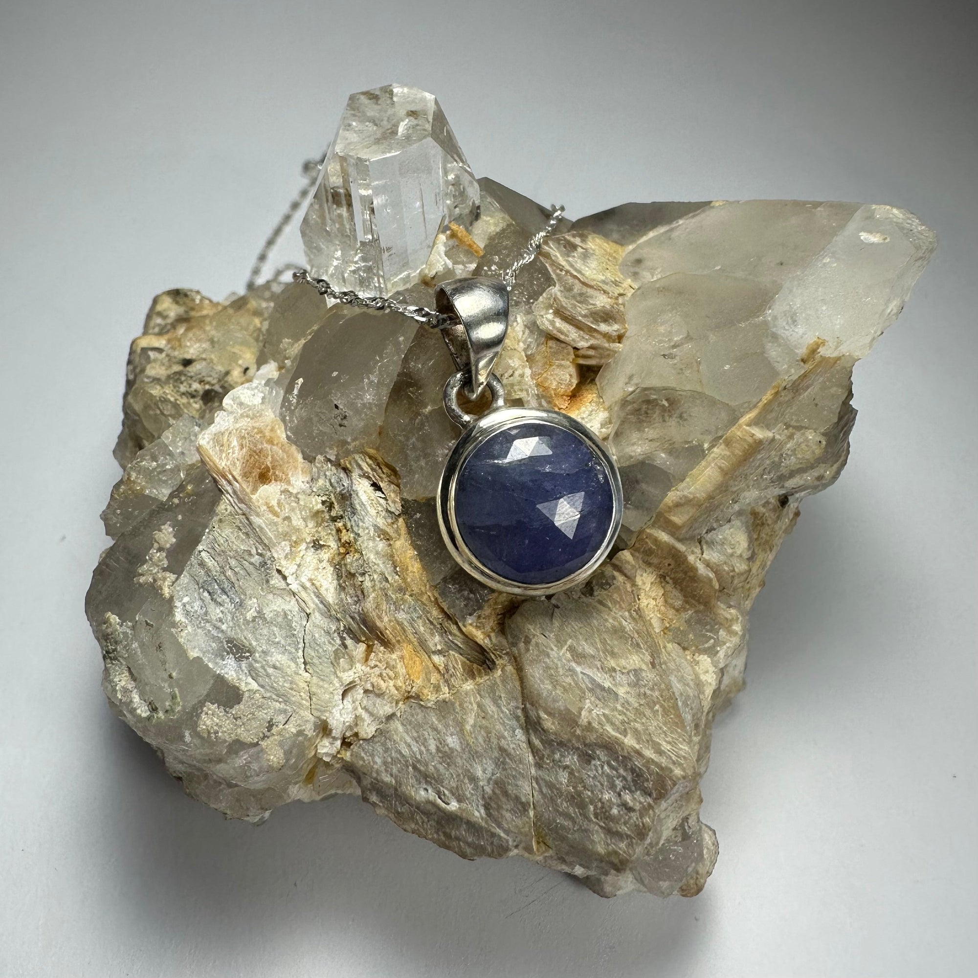 Round cut Tanzanite pendant with .925 Sterling Silver clasp displayed on a dark textured background