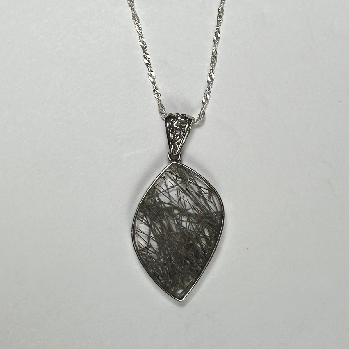 Marquise-shaped rutilated quartz pendant with black needle-like inclusions set in a silver bezel, hanging from a twisted silver chain on a neutral background.