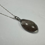 Teardrop-shaped silver pendant with brown rutile needles inside, hanging from a delicate twisted silver chain on a plain light gray background.