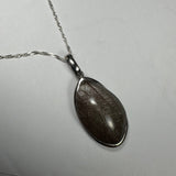 Teardrop-shaped silver pendant with a dark rutilated quartz stone featuring thin, intersecting needle-like inclusions on a twisted silver chain against a light background.