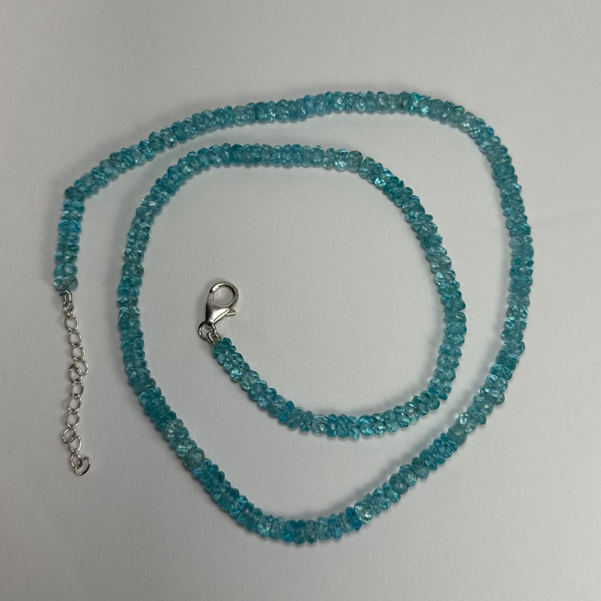 Delicate necklace composed of small translucent blue apatite beads with a silver lobster claw clasp and adjustable chain on a white background.
