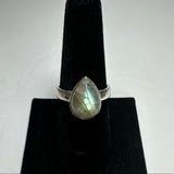 Teardrop-shaped labradorite ring with iridescent blue-green flashes set in a simple silver band on a black velvet ring stand.
