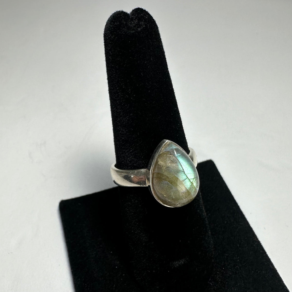 Teardrop-shaped labradorite stone with blue and gold iridescence set in a polished silver ring displayed on a black velvet ring holder.