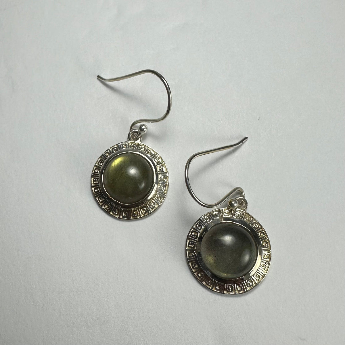 Pair of silver dangle earrings each featuring a round labradorite stone with an iridescent greenish-grey hue set in an intricately patterned silver bezel.