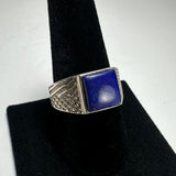 Square lapis lazuli stone set in a silver ring with textured geometric patterns on the band, displayed on a black velvet ring holder.