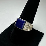 Silver ring with a square lapis lazuli stone center and detailed textured patterns on the band sides, displayed on a black velvet cone stand.