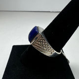 Silver ring with textured geometric pattern on the band, featuring a polished deep blue lapis lazuli stone, displayed on a black velvet ring holder.