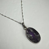 Oval pendant featuring a rough amethyst stone with deep purple and black inclusions set in a simple silver bezel on a delicate silver twisted chain.