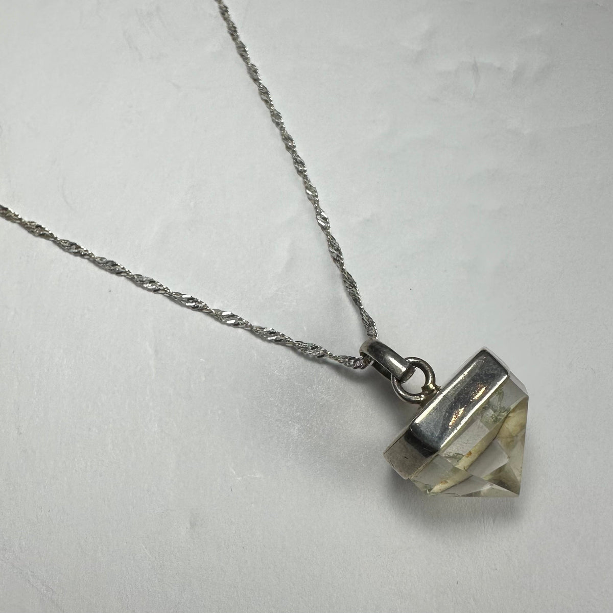 Clear quartz pendant with natural inclusions set in a silver-tone metal cap, hanging from a twisted silver chain on a white background.