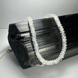 Close-up of translucent moonstone rondelle bead necklace draped over textured black tourmaline crystal on white background
